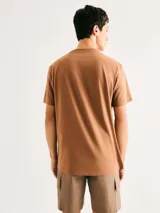 Camiseta blanca de algodón con cuello redondo y mangas cortas. Estampa rectangular con borde negro que contiene la frase "NATURAL ATMOSPHERE" en letras mayúsculas y una imagen de montañas y mar.