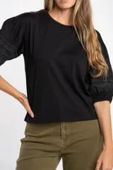 Remera negra de algodón con mangas cortas abullonadas que presentan detalles de encaje bordado y calado en los extremos.