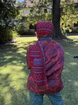 Balaclava tejida con diseño de capucha integrada y bufanda larga, confeccionada en una mezcla de algodón y acrílico con motivos geométricos en tonos rojo y azul.