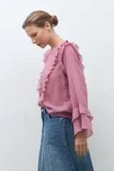 Blusa de manga larga color rosado con textura, escote redondo y volados decorativos en los hombros y a lo largo del frente.