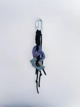 Charm para bolso o accesorios con mosquetón metálico, tejido de macramé en cordón negro y dijes de cerámica esmaltada en tonos violeta y celeste.