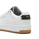 Championes Puma Court Classic de diseño urbano, color blanco con detalles en negro en la lengüeta y el talón. Presenta logo Puma en dorado en el lateral y la lengüeta, ojales superiores metálicos dorados y suela de goma color caramelo.
