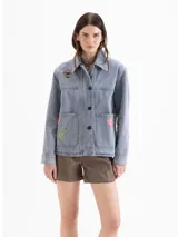 Chaqueta de denim de algodón color azul con efecto lavado, corte recto y cierre frontal con botones. Presenta bolsillos aplicados en el frente y bordados de una abeja y flores.
