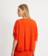 Blusa amplia color naranja, con escote en pico y mangas cortas con detalle de lazo fruncido.