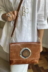 Sobre de cuero color marrón con solapa frontal decorada con una piedra de ágata natural engarzada en metal. Incluye correa larga ajustable y extraíble para usar como bandolera.