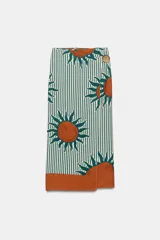 Falda midi estilo pareo con diseño cruzado, estampado de rayas verticales en tono verde oscuro y blanco, combinado con grandes motivos de soles naranjas y verdes, y cierre lateral con botón.
