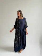 Vestido largo azul oscuro con diseño asimétrico que combina un lado liso con un lado estampado de hojas, manga corta y bolsillo frontal aplicado.