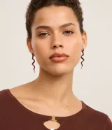 Aros colgantes medianos con forma de serpiente, esmaltados en color marrón y blanco con detalles dorados.