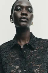 Camisa de encaje negro con cuello solapa, manga corta y cierre frontal con botones.