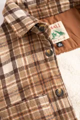 Camisa leñadora marrón a cuadros con forro de corderito sintético, cierre con botones y dos bolsillos frontales con tapa.
