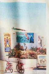 Remera oversized de algodón color blanco hueso con cuello redondo, manga corta y hombros caídos. Presenta un estampado fotográfico vintage en el centro que muestra la fachada de un local con carteles y dos bicicletas estacionadas, con el texto "Fiesta Hollywood Party, 1974" y el logo "Pacha" en rojo.