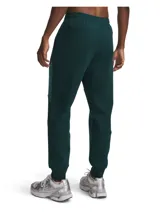 Pantalón de jogging Under Armour, modelo Unstoppable, en color verde oscuro. Presenta un diseño de doble punto con paneles en contraste, cintura elástica con cordón interno, bolsillos laterales abiertos y un bolsillo lateral con cierre. Corte ajustado en las piernas.