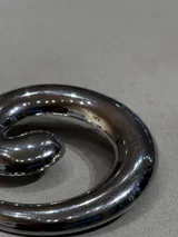 Pin metálico con diseño de espiral en acabado plateado brillante, ideal para personalizar prendas y accesorios.