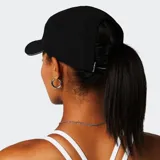 Gorro deportivo tipo gorra de cinco paneles, color negro, con logo reflectante en el frente y borde reflectante en la visera. Diseñado con una abertura trasera específica para coleta, fabricado en tejido técnico ligero, transpirable, de secado rápido y resistente al agua.