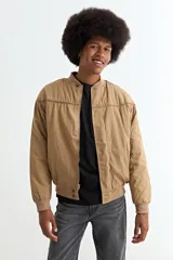 Campera tipo bomber color tostado, con cierre frontal, cuello, puños y ruedo de tejido elástico acanalado. Presenta costuras horizontales en la parte superior del pecho.