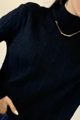 Buzo de hilo de punto con diseño de trenzas verticales, cuello alto y cadena metálica decorativa incorporada en la parte frontal.
