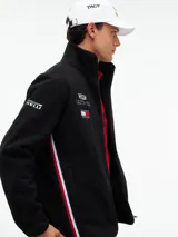 Campera de tejido polar negra Tommy Hilfiger, con cuello chimenea y cierre de cremallera. Presenta diseño Global Stripe en los laterales, bolsillos abiertos en diagonal y el logo de la marca junto con el de Cadillac Formula 1 Team en el pecho.