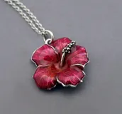 Collar con dije de flor de hibisco esmaltada en tonos rojizos/fucsia, con detalles plateados en el centro de la flor y cadena de eslabones plateada.