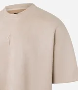 Remera oversized color beige confeccionada en gamuza sintética. Presenta cuello redondo, mangas cortas y bordado de cruz en el frente.