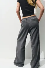 Pantalón gris oscuro a rayas verticales finas, de corte holgado, con elástico y cordón ajustable en la cintura, bolsillos laterales y bolsillos decorativos en la parte trasera. Confeccionado en sarga.