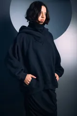 Buzo negro de corte oversize con cuello alto tipo polera y capucha integrada. Presenta mangas largas con puños ajustados y un diseño holgado en el cuerpo.