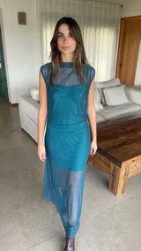 Vestido largo de microtul bordó, sin mangas, con escote alto tipo buche y diseño transparente con forro corto interno que genera un efecto translúcido en la falda.