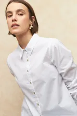 Camisa de algodón blanca con cuello clásico, cierre frontal abotonado con botones de nácar y mangas largas con puños definidos.