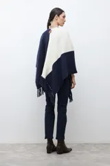 Ruana de tejido de punto con diseño color block en tonos crudo, gris y negro, con terminación de flecos en el ruedo y textura en relieve.