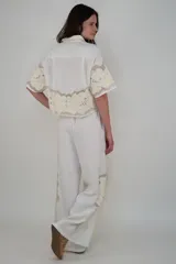 Pantalón blanco de lino con cintura elastizada, cordón de ajuste, bolsillos laterales y apliques de flores bordadas en los laterales.