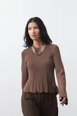 Top de tejido acanalado con sutil acabado metalizado, de silueta entallada con diseño peplum en la cintura y mangas largas levemente acampanadas.