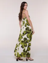 Vestido maxi de fondo blanco con estampado de flores grandes en tonos verde y marrón, con escote en V, breteles finos y detalle de abertura cut-out en el centro del busto.