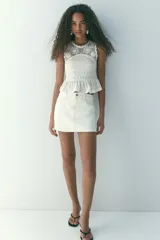 Short pollera de cinco bolsillos en denim de algodón color blanco, con diseño de tiro alto, cierre frontal y botón metálico.