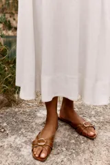 Sandalia plana color marrón con tiras cruzadas y detalle metálico dorado en la parte delantera.