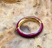 Set de pulseras rígidas de diferentes colores y materiales, incluyendo una pulsera dorada tipo brazalete y pulseras de resina en verde, negro, naranja y borgoña, con detalles dorados.