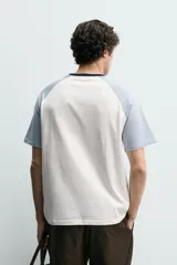 Camiseta de hombre regular fit, color blanco con mangas raglán cortas en azul claro y cuello redondo en rib azul marino.