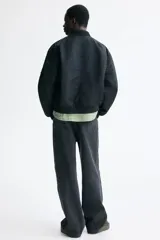 Campera bomber de nylon color negro, con cuello, puños y bajo acanalados. Presenta cierre frontal, bolsillos laterales con botón a presión y un bolsillo con cierre en la manga.