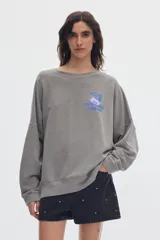 Buzo de felpa gris con efecto washed, cuello redondo, mangas largas y fit relajado. Presenta estampa gráfica en el pecho con texto en tonos azul y lila.