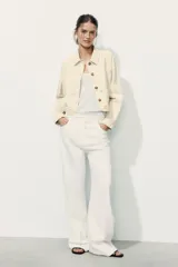 Cazadora color rosa pálido, de cuello solapa y manga larga. Tiene bordados perforados a tono en el ruedo y cierre frontal con botones color madera.