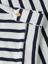 Remera de algodón con rayas horizontales azul marino y blancas, cuello redondo y mangas cortas con detalle enrollable y botón dorado. Presenta un pequeño logo bordado en el pecho.