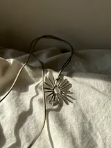 Colgante con dije en forma de sol con rayos, hecho a mano en alpaca, con cordón de gamuza marrón.