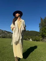 Ruana color crema tejida en lana merino, con flecos y bolsillos frontales.