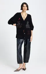 Cardigan negro de punto con escote en V y cierre frontal de botones. Presenta mangas tres cuartos y bolsillos frontales. El diseño destaca por sus bordados coloridos con motivos de cerezas y frases en francés distribuidas por toda la prenda.