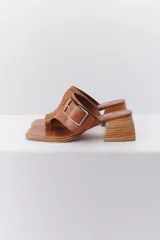 Sandalia color beige con tira ancha de cuero sobre el empeine, hebilla metálica plateada y taco geométrico de madera.