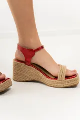 Sandalias de taco chino con plataforma revestida en yute natural. Posee capellada de tiras cruzadas de yute en la parte delantera, puntera cuadrada y tira ajustable de cuero rojo metalizado en el talón.