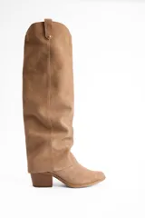 Bota de caña alta confeccionada en cuero vacuno, con diseño versátil que permite doblar la caña. Presenta un taco cuadrado de altura media y punta redondeada.