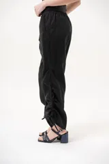 Pantalón negro de tiro medio con cintura elástica ajustable con cordón y detalles de fruncido con tiras en los laterales de las piernas.