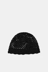 Gorro tipo casquete negro de crochet con tejido calado y apliques de flores en relieve en un lateral.