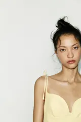 Vestido corto color amarillo pálido, con escote corazón, tirantes finos ajustables con detalle de lazos y falda acampanada.