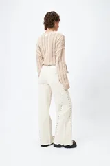 Pantalón de denim corte wide leg color marrón, con ruedo desflecado y detalle de tachas metálicas a lo largo de las costuras laterales.