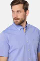 Camisa sport lisa de manga corta en color celeste, con cuello abotonado, cierre frontal con botones, bolsillo en el pecho y etiqueta decorativa en el ruedo.